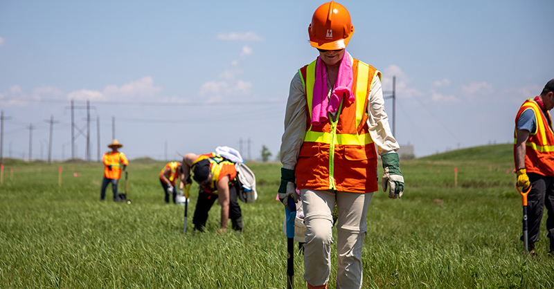 SaskPower employees in a grassy field wearing orange hard hats and vests planting trees.