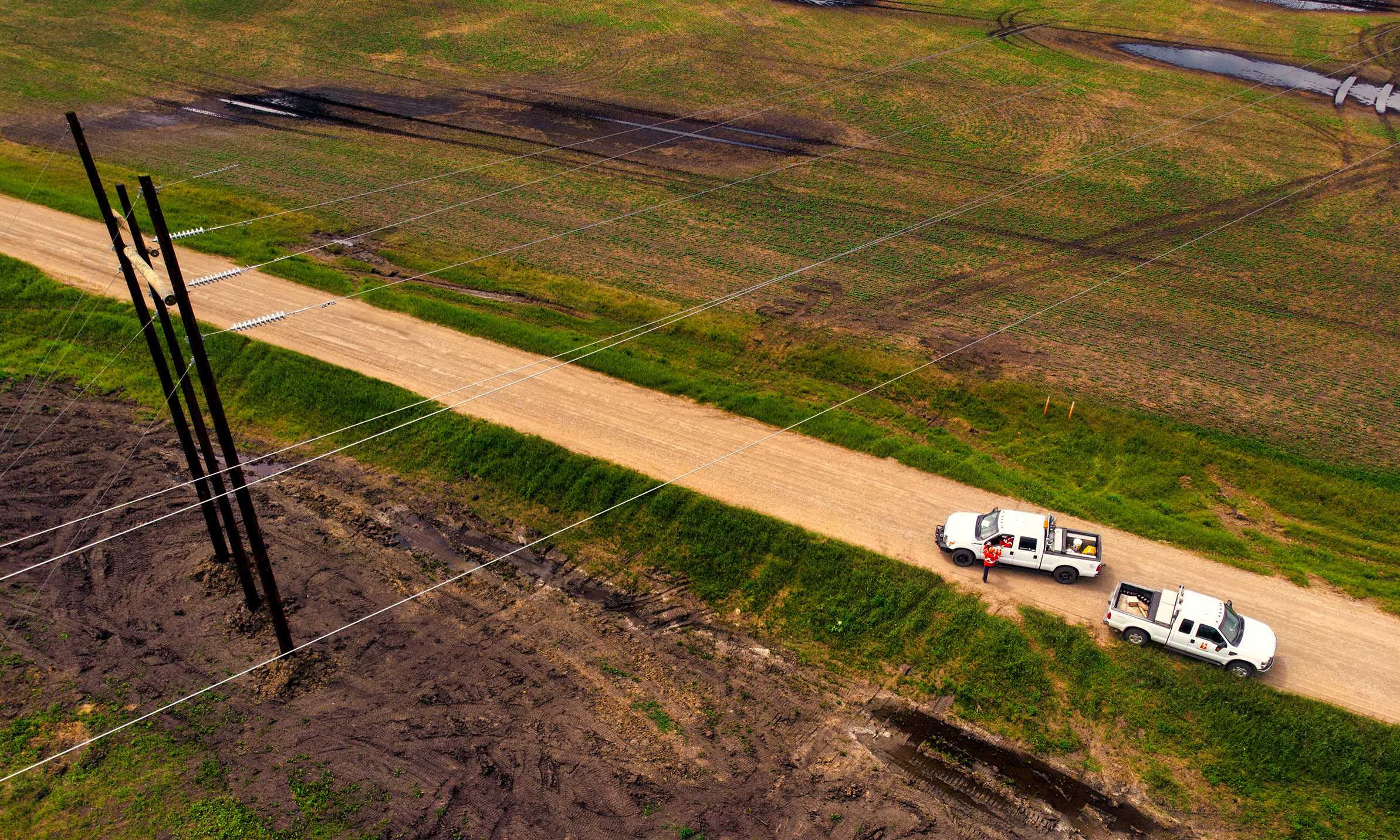 Ariel view of transmission lines with 2 SaskPower trucks on a grid road