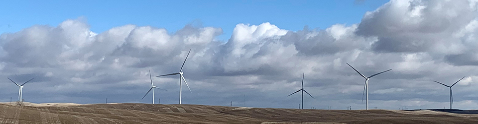 A row of large wind turbines in a field with clouds behind.