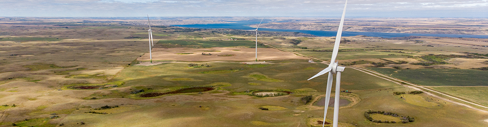 An aerial view of three white turbines with green grass and a lake below. 