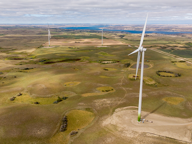 An aerial view of 3 white wind turbines with green space and a lake. 