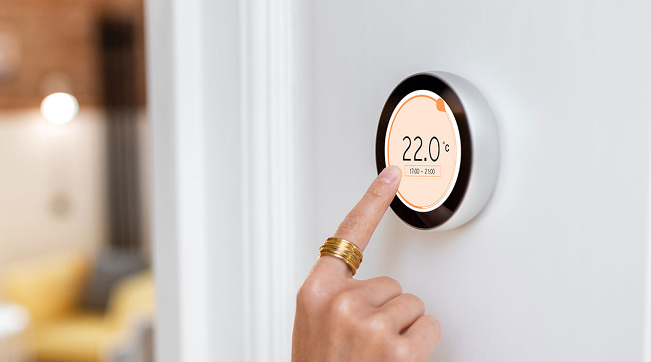A hand wearing a gold ring adjusting the temperature on a smart thermostat. 