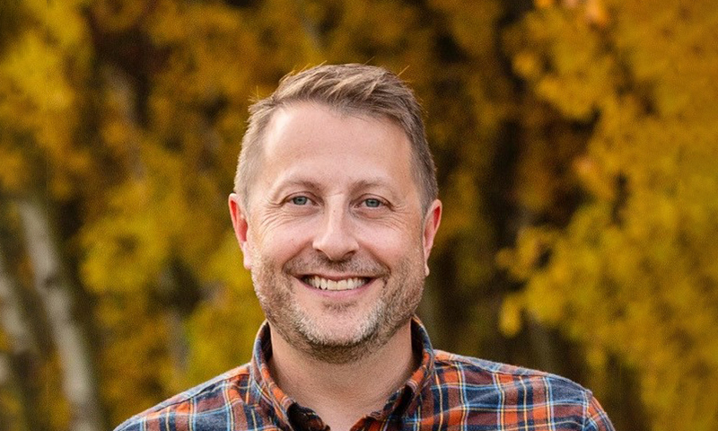 Doug Opseth smiling in front of a green background.
