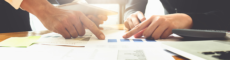 Two people's hands pointing to papers with charts and tables.