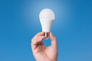 a hand holding up a light bulb on a blue background. 