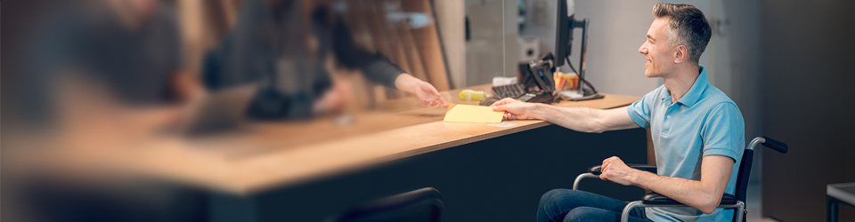 a man in a wheelchair getting assistance from an employee behind the desk